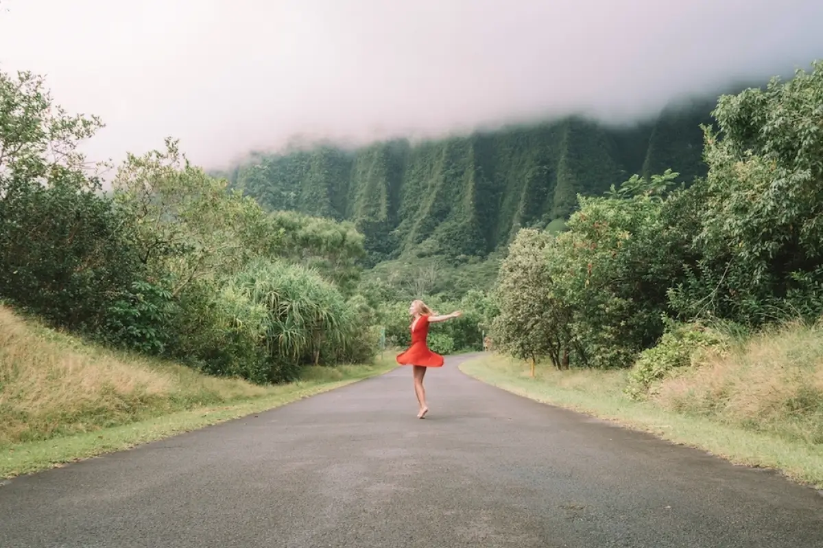 Woman dancing in the middle of an empty road surrounded by trees