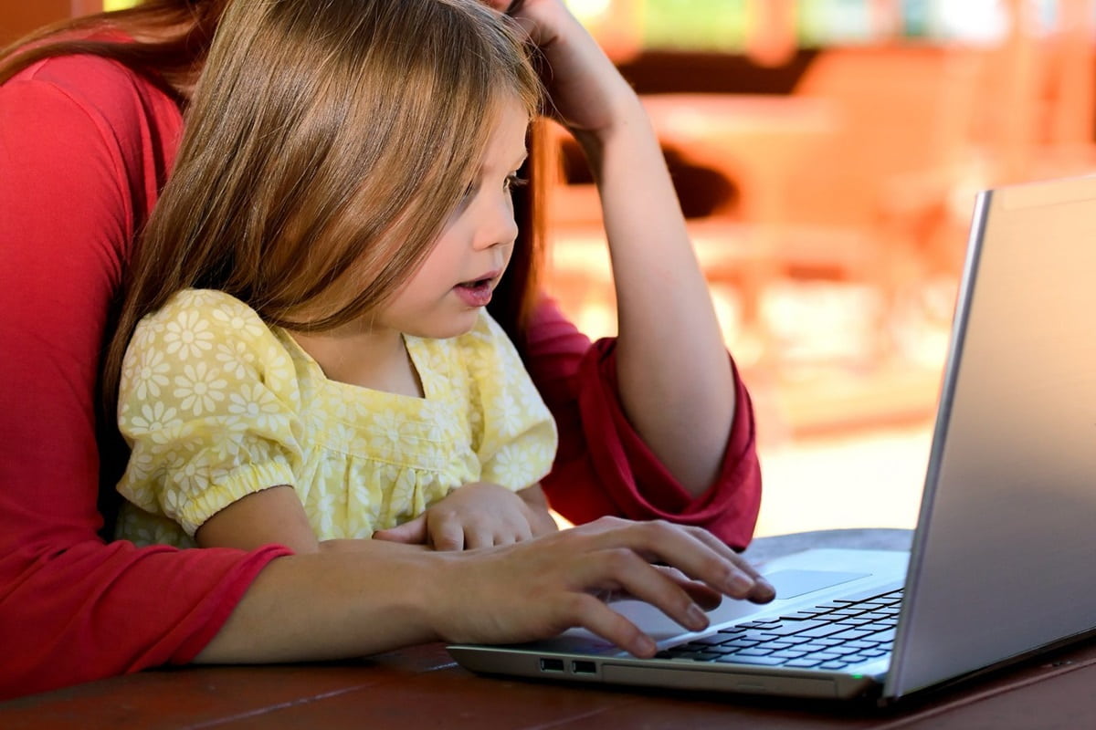 woman balancing her daughter on lap while using laptop