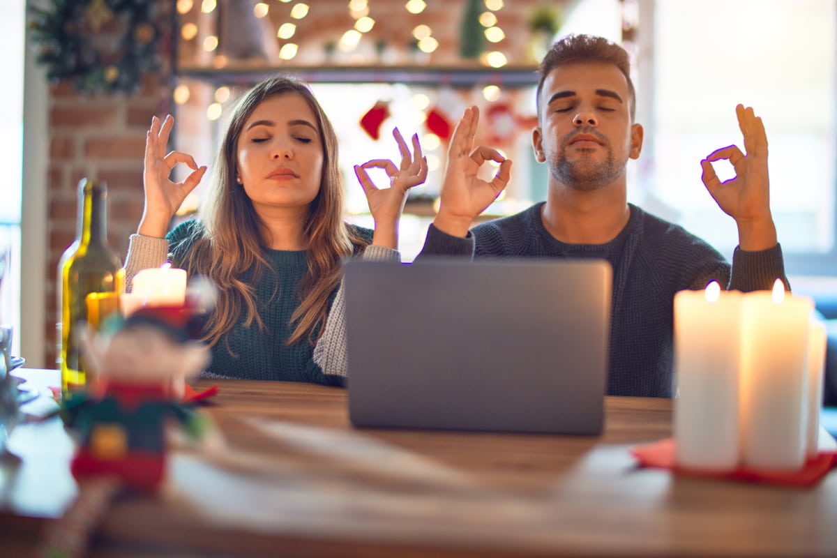 Unstressed couple using laptop around holiday decorations doing meditation