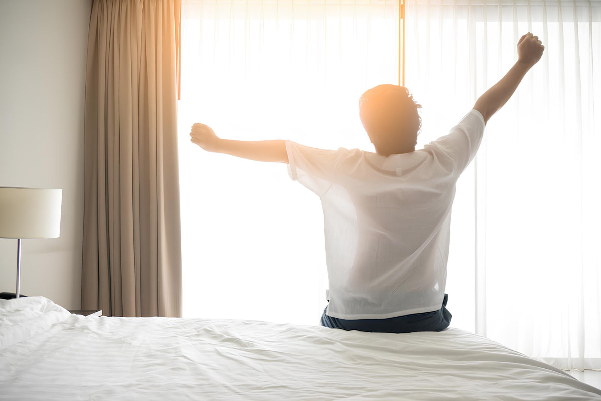 Man stretching on the bed towards sunrise window