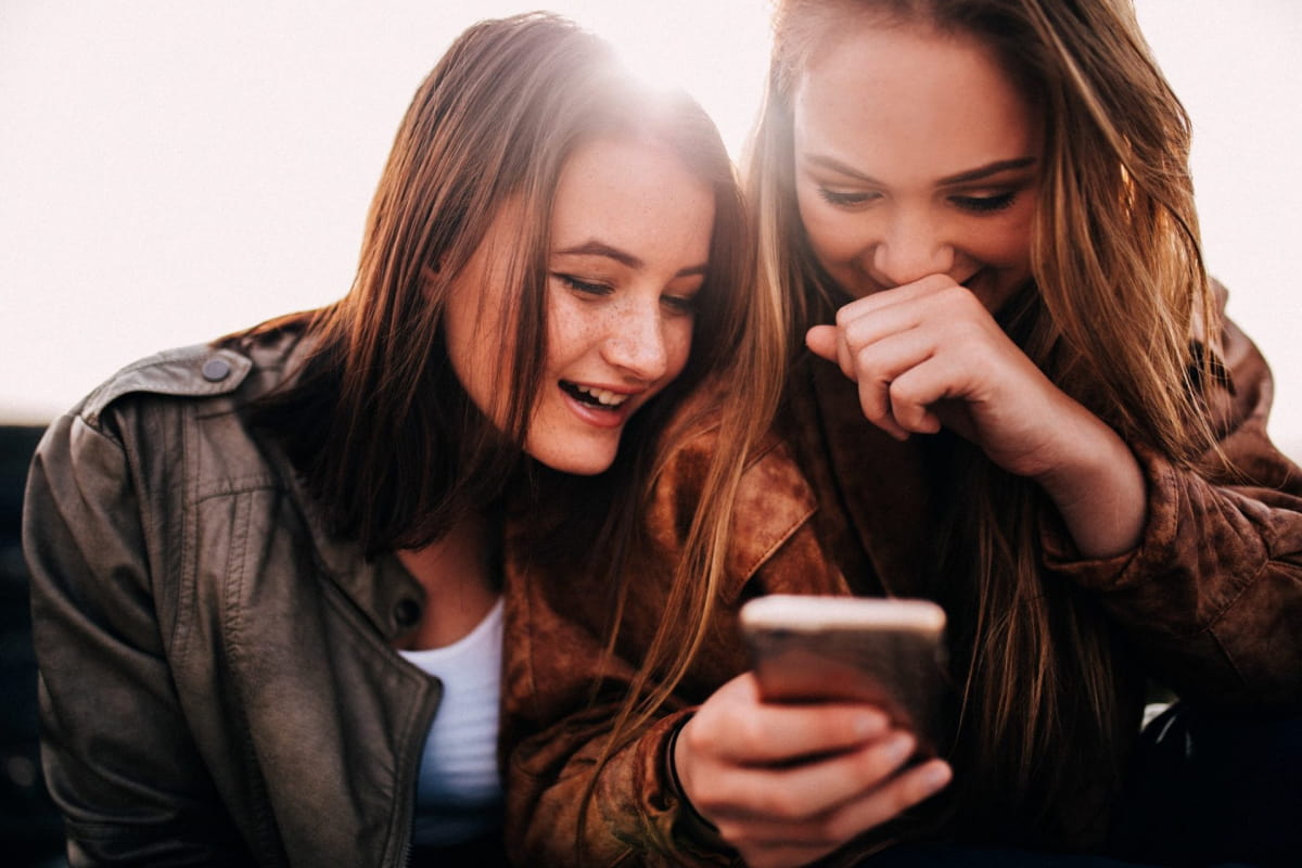 teenage girls looking at funny photos on smartphone and laughing