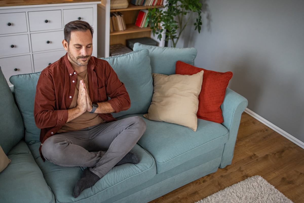 Middle aged man practicing meditation at home sitting on sofa