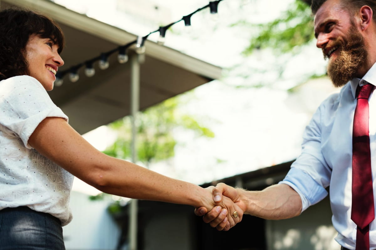 Woman and bearded man wearing red tie shaking hands