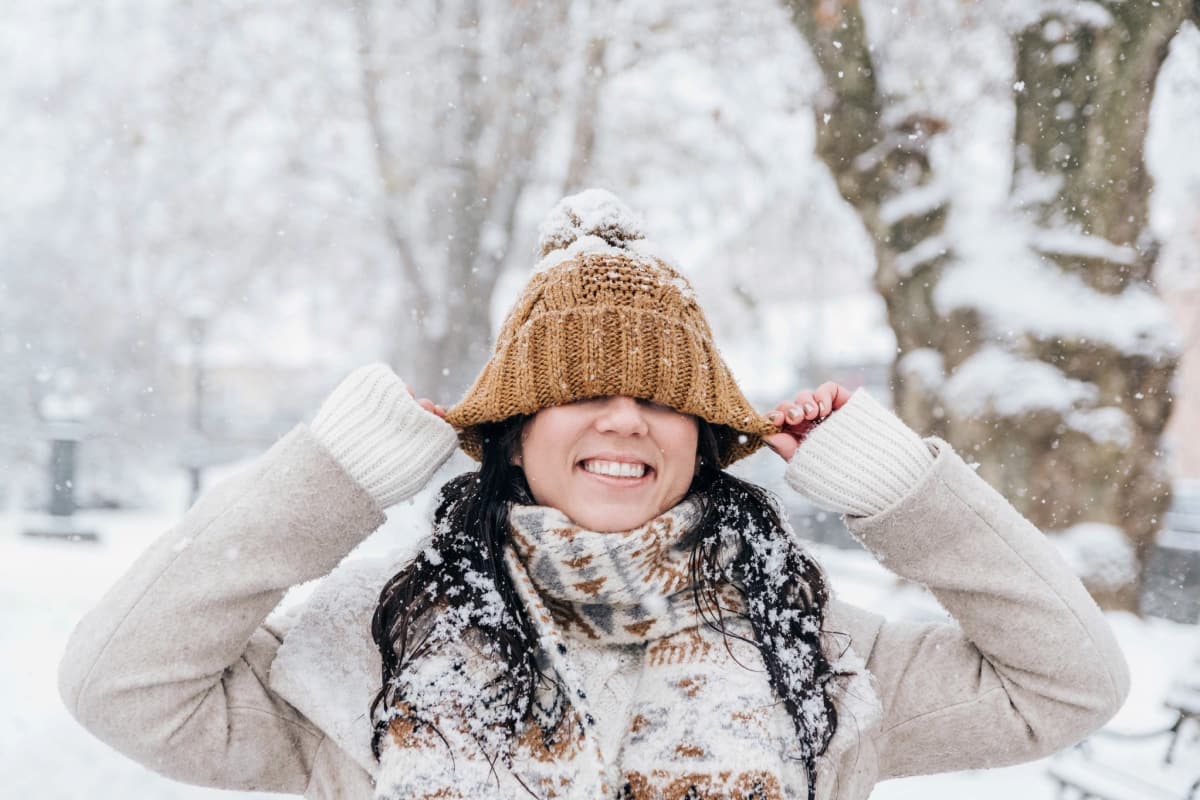 woman pulling brown hat tight over head in snow