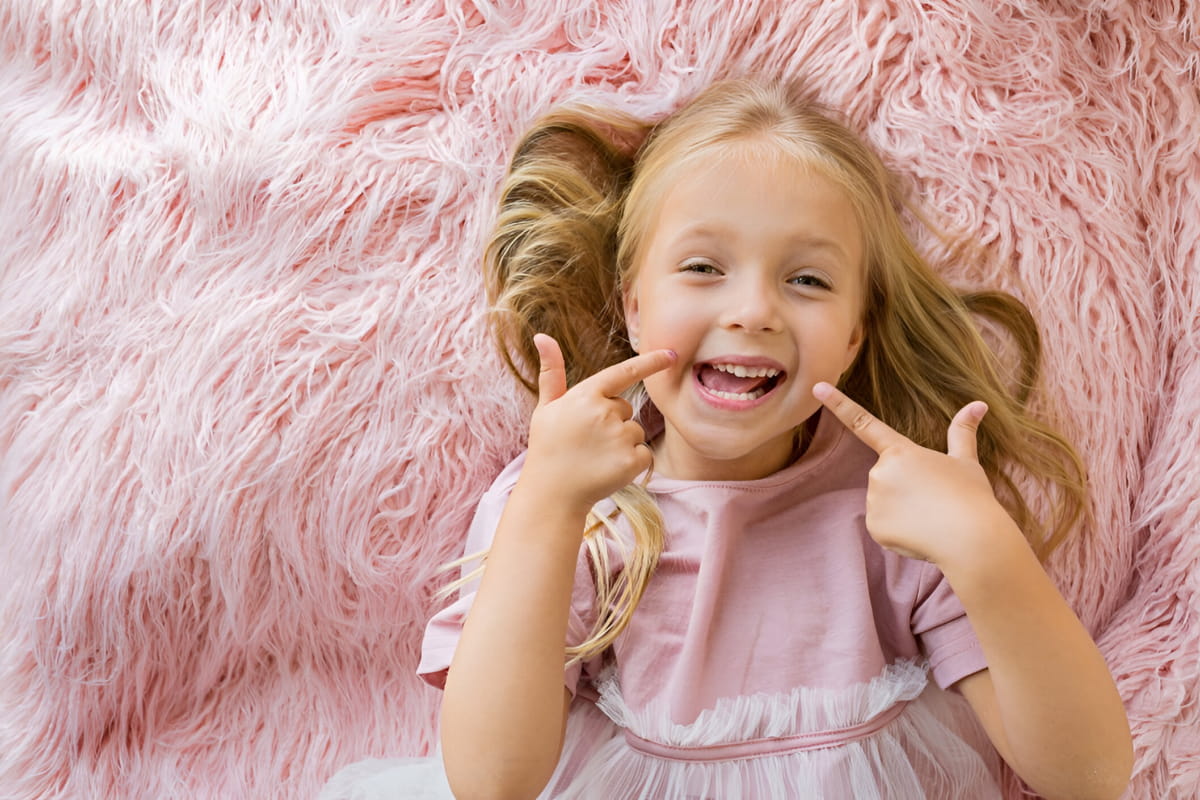 Young girl smiling while laying on fluffy pink bed