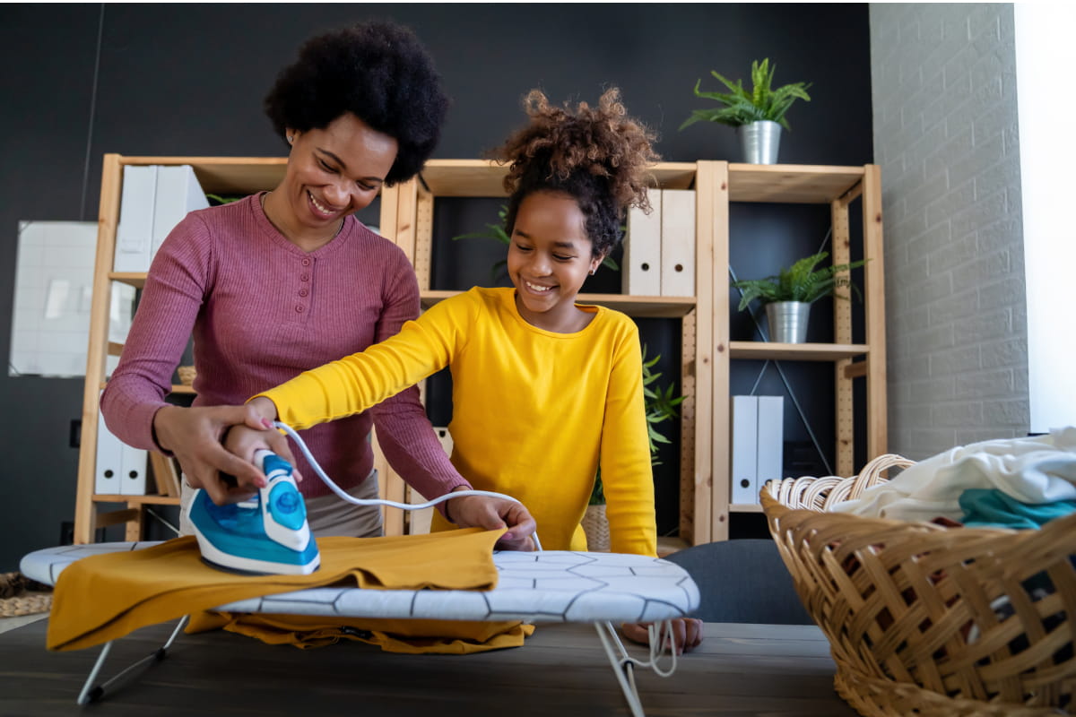 mother teaches daughter independence by showing her how to iron clothes