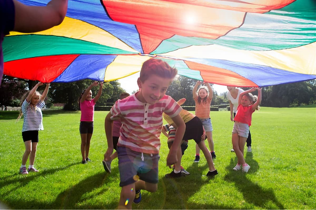 Children playing outside under rainbow parachute