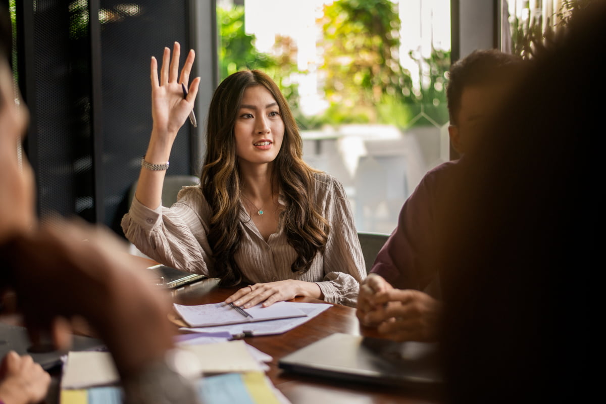 Asaian business woman raising hand speaking up during a discussion